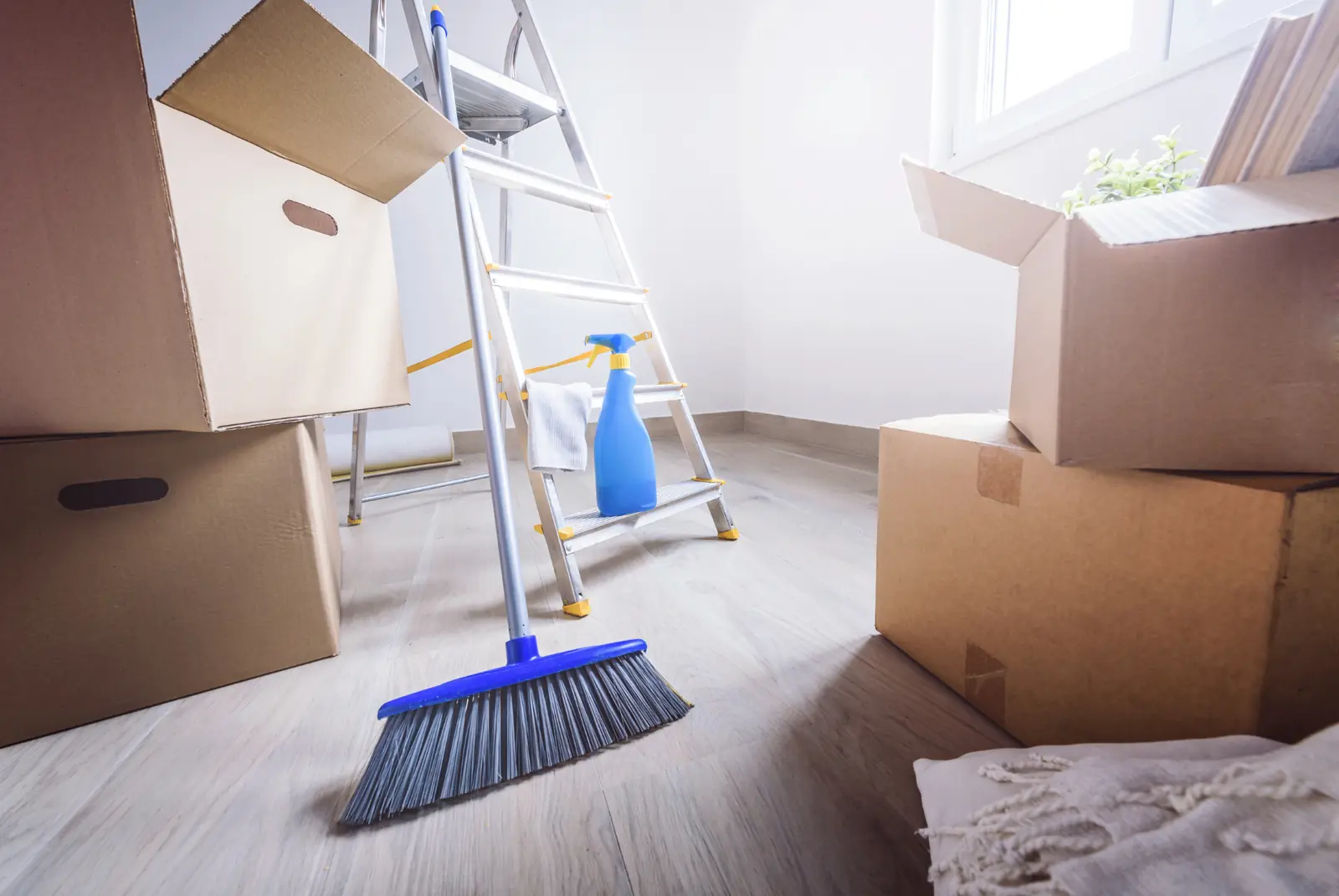 Broom and cleaning supplies among moving boxes in an empty room